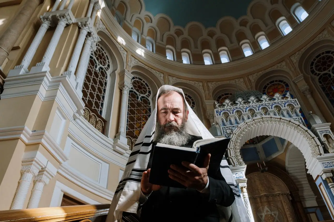 A rabbi in traditional Jewish attire reads the Torah inside a beautifully ornate synagogue